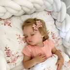 baby sleeping next to white double braided crib bumper floral sheet