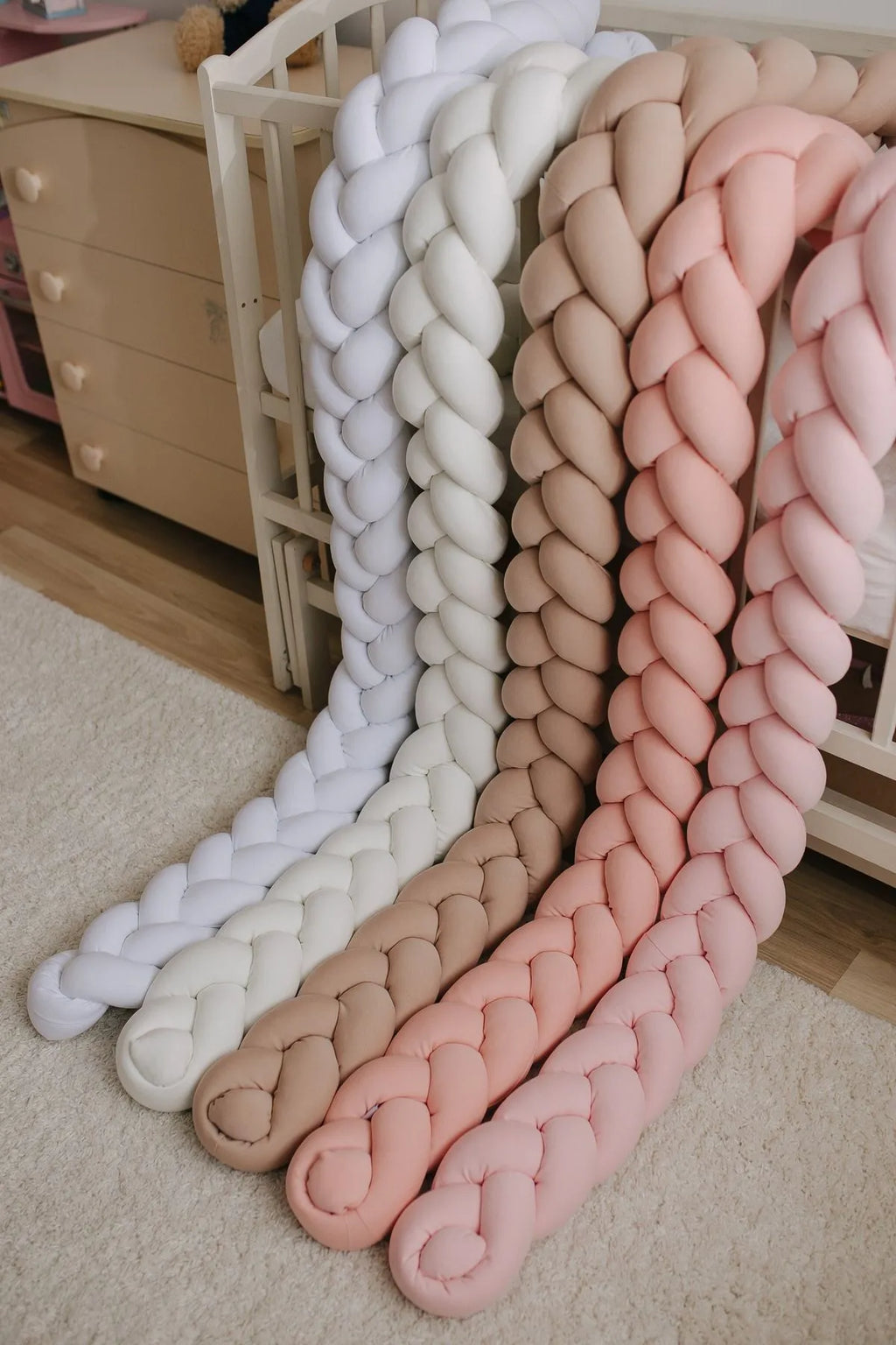 3-strand braided crib bumpers in white, ivory, beige and pink tones against wooden crib, handmade cotton bumpers CottonNest