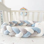Braided crib bumper in pastel colors on a crib with a rainbow toy in the background.