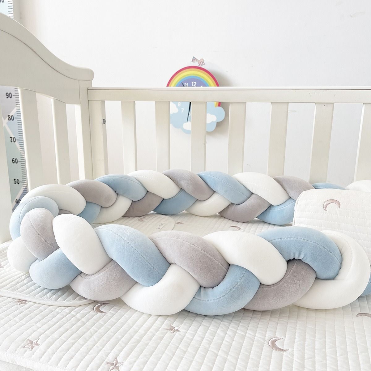 Braided crib bumper in pastel colors on a crib with a rainbow toy in the background.