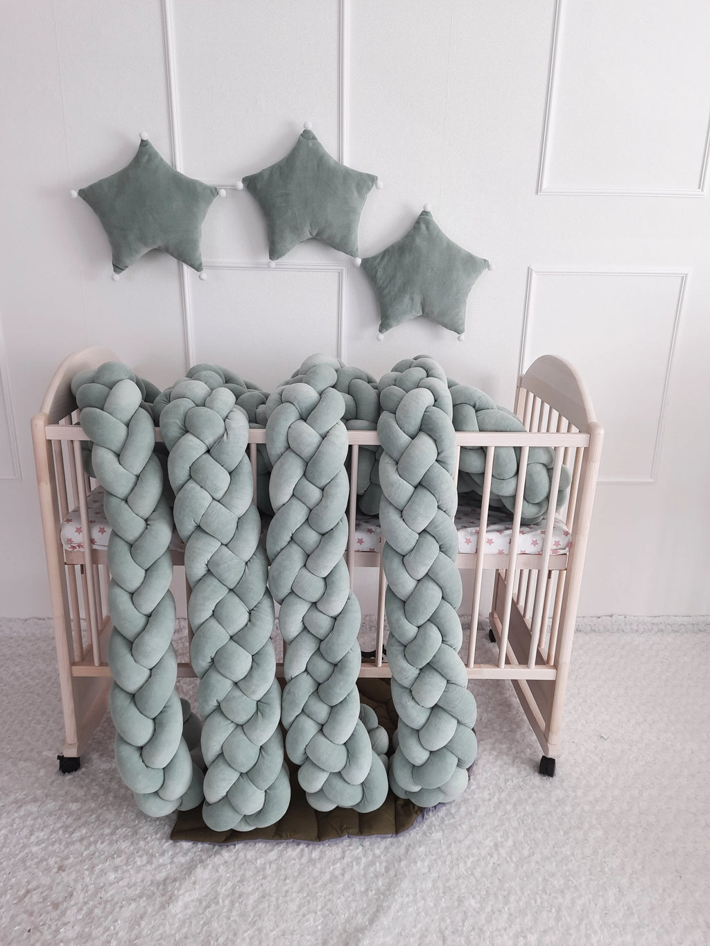 solid sage green 4 strand braided crib bumper draped over natural wood crib, nature nursery decor