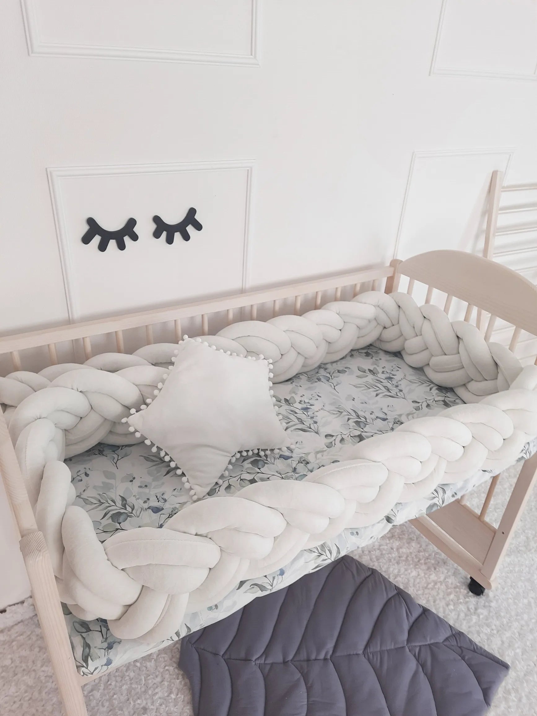 cream braided crib bumper in wooden crib with floral sheet neutral nursery