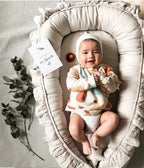 Smiling baby in beige ruffled organic cotton baby nest, handmade newborn lounger with eucalyptus decor