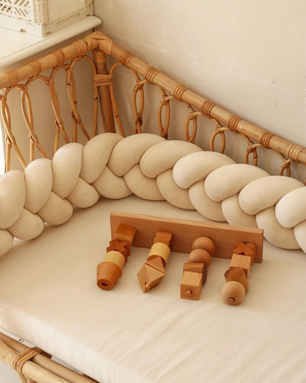 Beige 3-strand braided crib bumper in rattan crib with wooden toys, organic cotton nursery decor