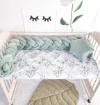 sage green woven crib bumper in wooden crib with botanical sheet