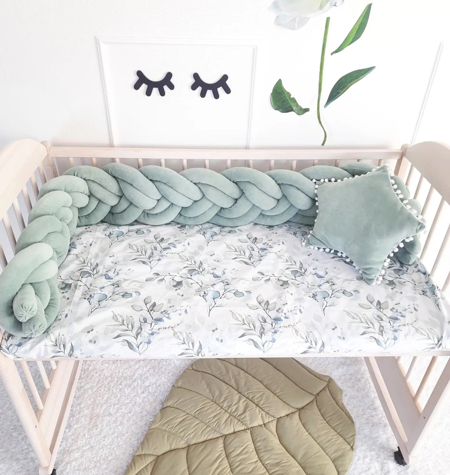 sage green woven crib bumper in wooden crib with botanical sheet