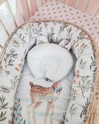 Top view of cotton baby nest with deer print inside crib, soft handmade newborn lounger with pillow