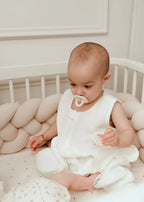 baby sitting in white round crib with solid cream 4 strand braided bumper, OEKO-TEX cotton, hypoallergenic