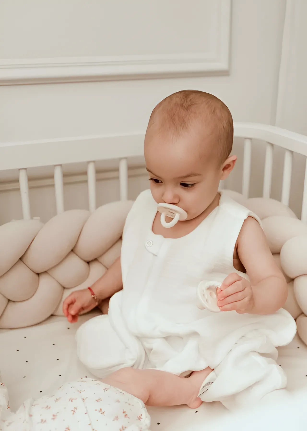 baby sitting in white round crib with solid cream 4 strand braided bumper, OEKO-TEX cotton, hypoallergenic