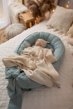 Newborn in blue organic baby nest with muslin blanket, OEKO-TEX certified linen baby lounger