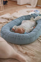 Baby resting in blue organic baby nest on floor, breathable linen baby lounger, CottonNest