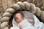 newborn sleeping in rattan bassinet with beige braided crib bumper, safe for newborns