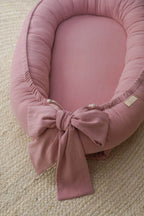 Close-up of decorative bow on pink linen baby nest, handmade detail, newborn girl baby lounger