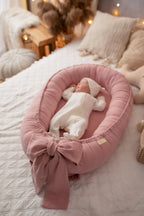 Newborn sleeping in light pink linen baby nest with bow, organic baby girl lounger, pink nursery