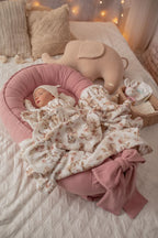 Newborn in pink organic baby nest with floral muslin blanket and elephant toy, safe hypoallergenic baby girl lounger