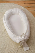Ivory linen baby nest top view on round rug, cream organic baby lounger with decorative bow, CottonNest