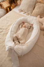 Newborn sleeping in ivory linen baby nest with bow, cream organic baby lounger, classic nursery decor