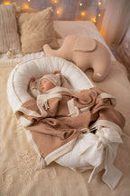 Baby in ivory organic cotton baby nest with muslin blanket and elephant toy, cream newborn lounger