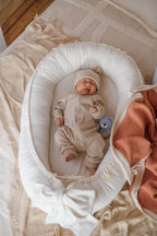 Smiling newborn in cream organic baby nest, top view, ivory linen baby lounger, neutral nursery