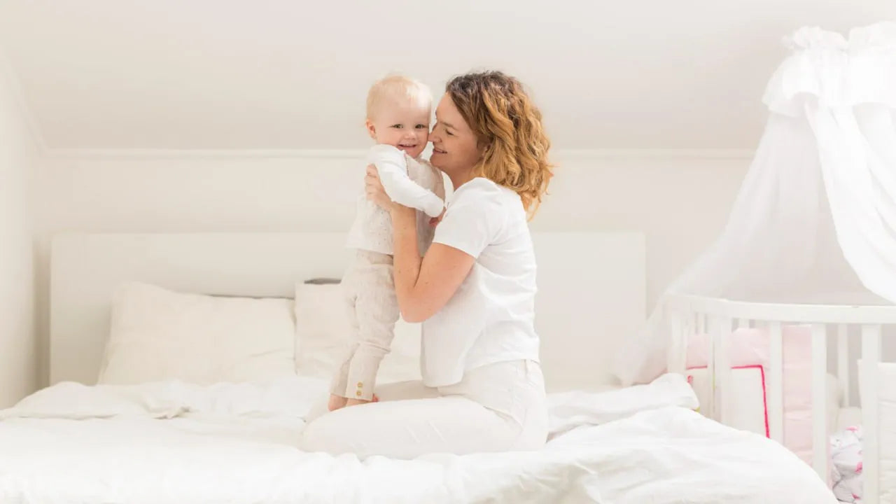 mother holding smiling baby white nursery room crib bumper background